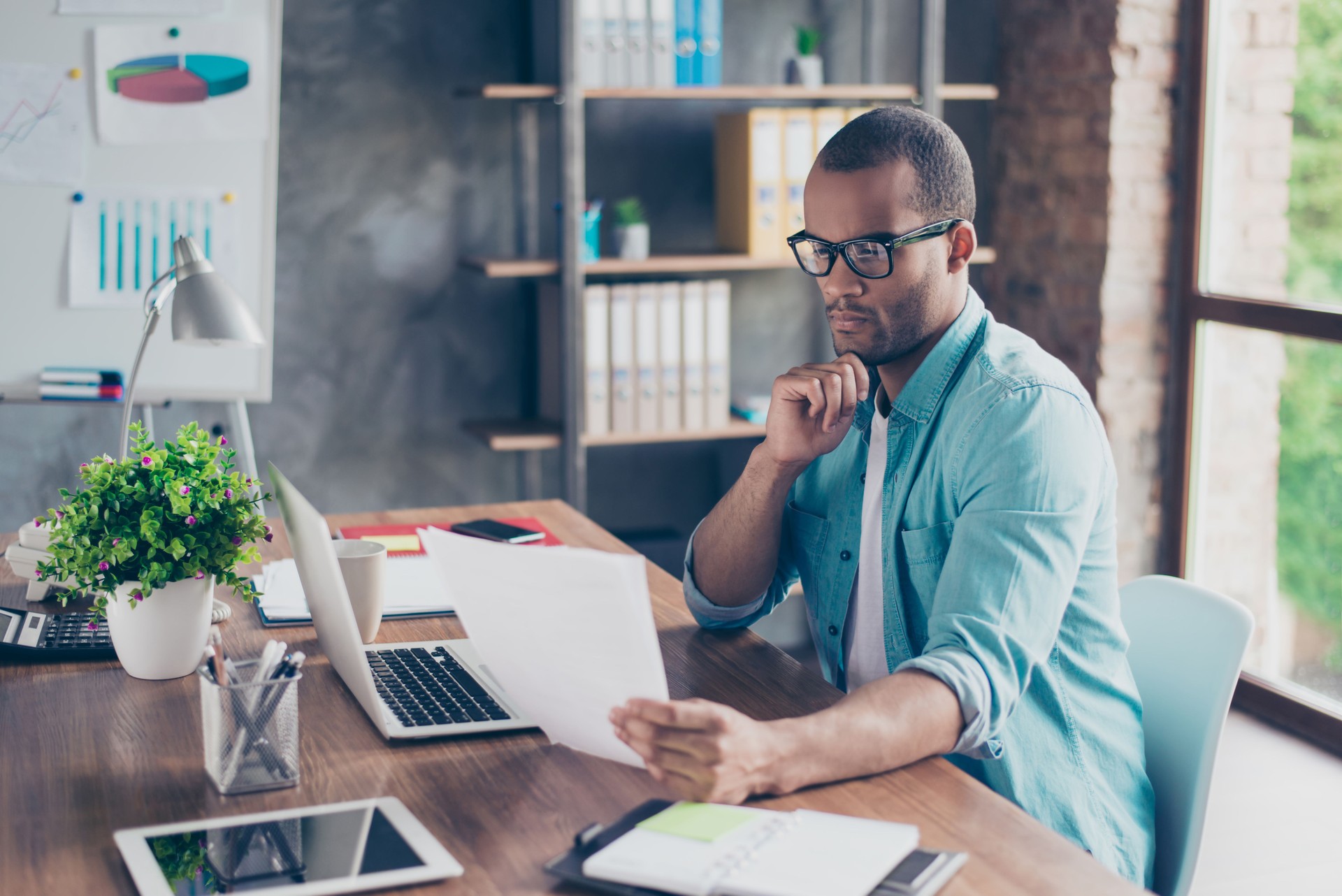 So nerd and focused. Young handsome afro student is concentrated on studying. He is in a casual outfit with project at his work station